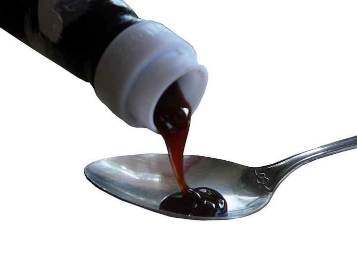 Dark brown oyster sauce poured from a bottle onto a spoon