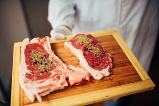 Two raw seasoned pork chops on a wooden board