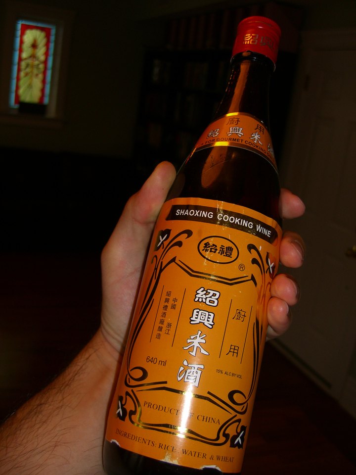 A hand holding a bottle of Shaoxing cooking wine with a gold and orange label